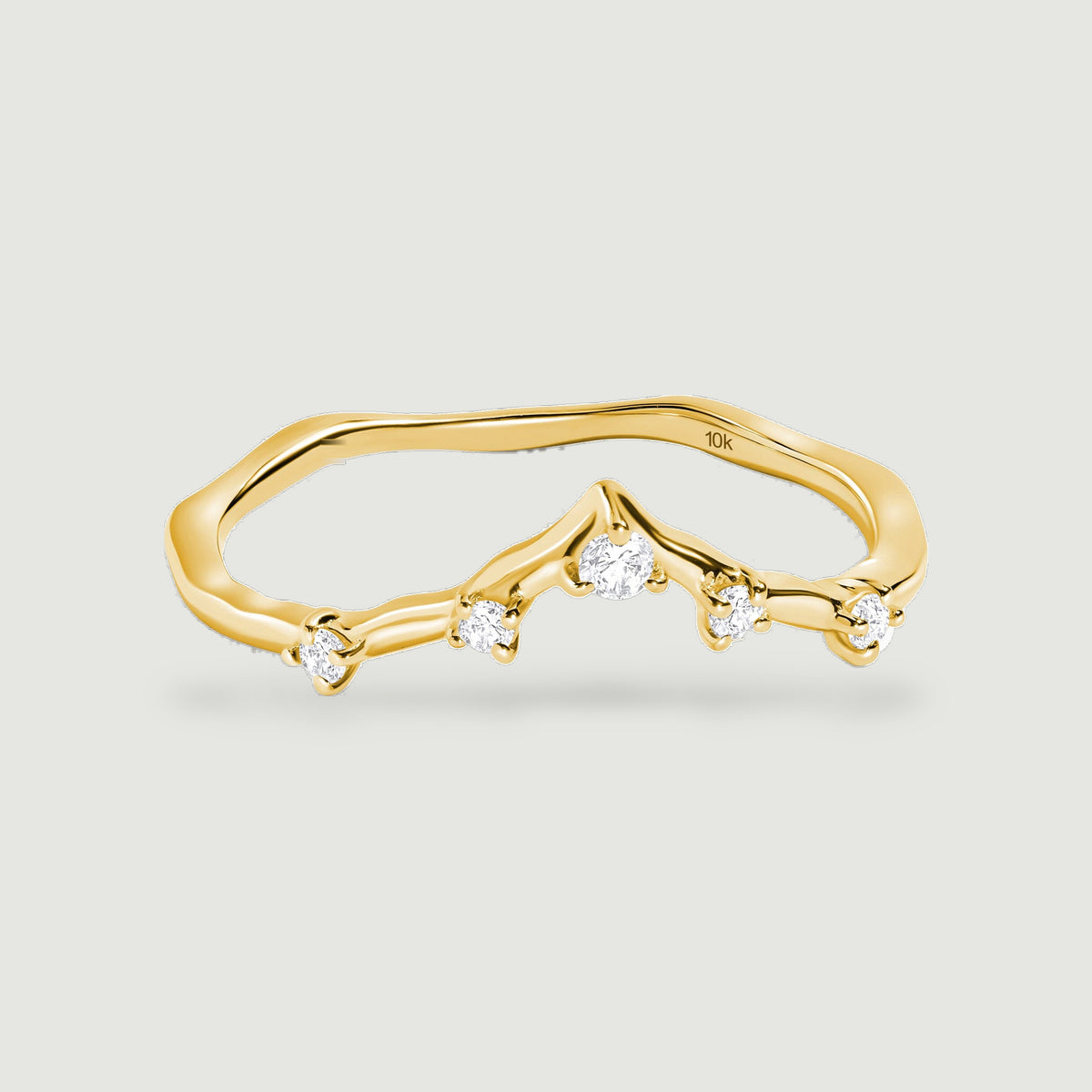 A polished yellow gold ring with five round diamonds and a curved V-shaped band rests on a pale gray surface.