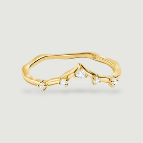 A polished yellow gold ring with five round diamonds and a curved V-shaped band rests on a pale gray surface.