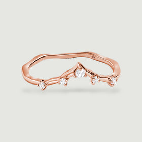 Five clear round diamonds follow the curved front of a rose gold ring against a light gray background.