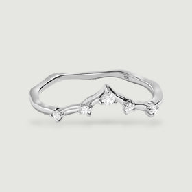 A white gold diamond ring is shown from a low front angle with its slender band and raised central point visible.