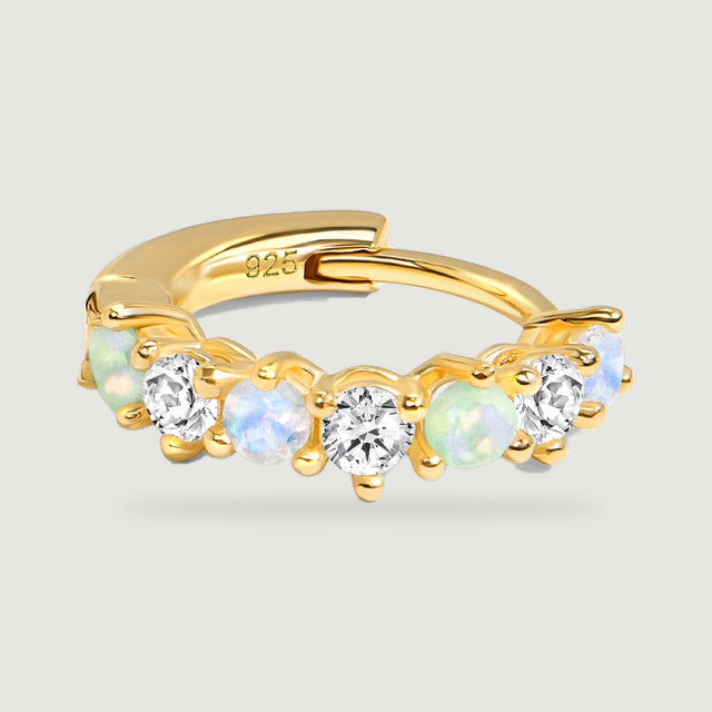 A yellow gold hoop lies flat with its hinged back and row of colored and clear stones facing forward.