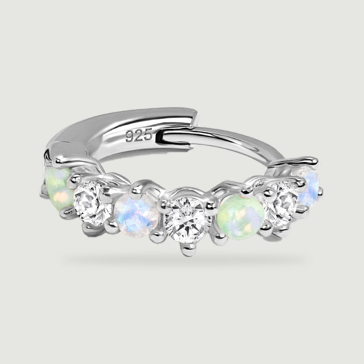 A silver hoop rests horizontally, showing rounded prongs and alternating blue, green, and clear stones.