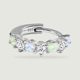A silver hoop rests horizontally, showing rounded prongs and alternating blue, green, and clear stones.