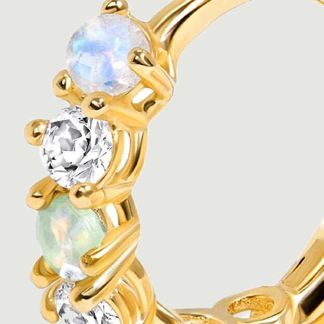 A close view shows pale blue, clear, and green round stones held by polished yellow gold prongs.