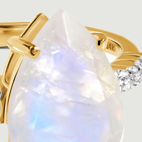 A close view reveals the pointed moonstone tip, polished gold prongs, and a row of round diamonds.