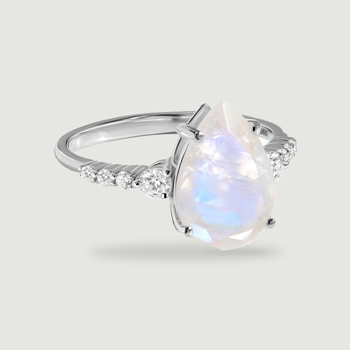 A pear-shaped moonstone ring in white gold sits above a soft shadow on a light gray surface.