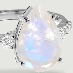 A close view shows the faceted moonstone, white gold prongs, and round diamonds along the ring shoulders.