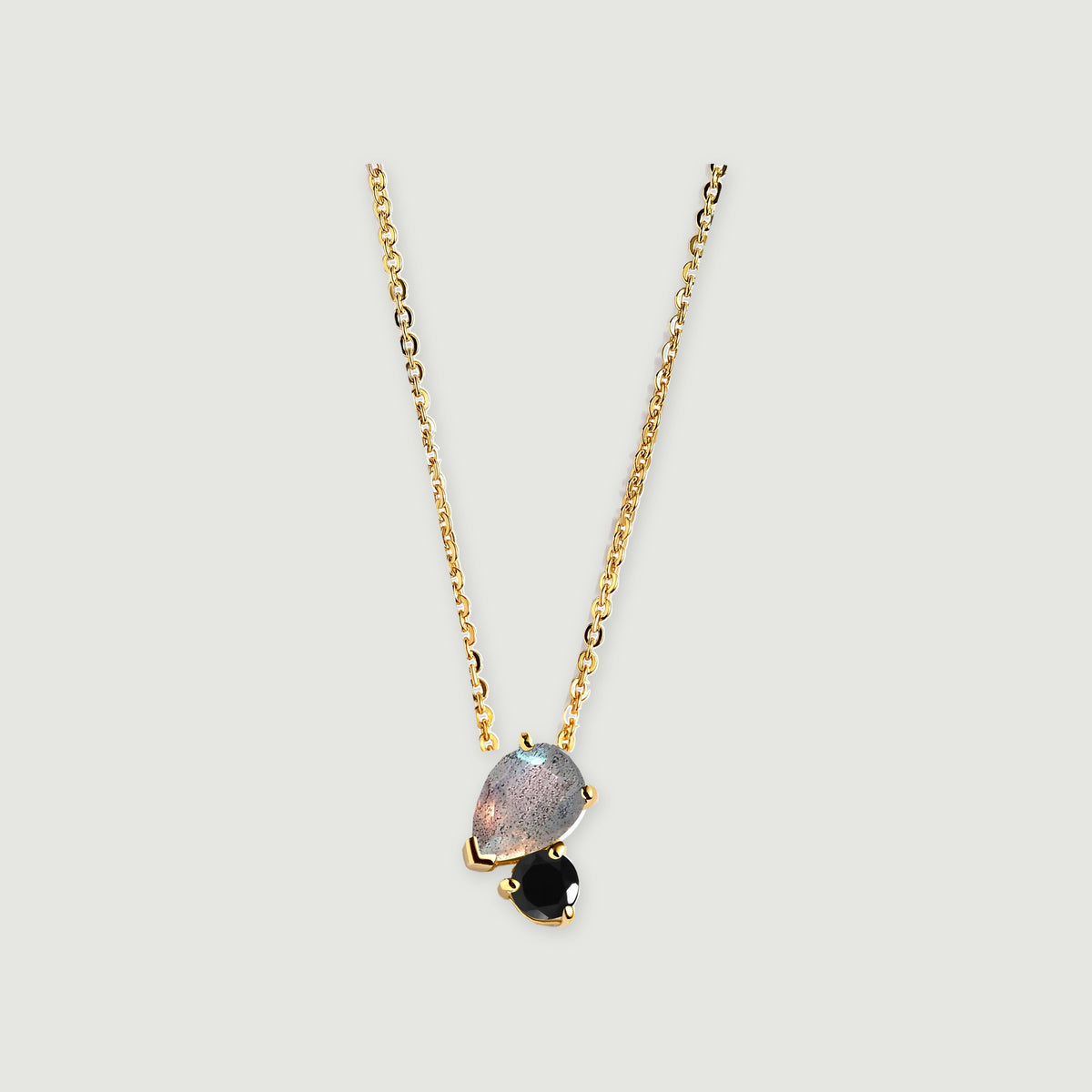 A yellow gold chain leads to a gray pear-shaped stone and a smaller black round stone with polished gold prongs.
