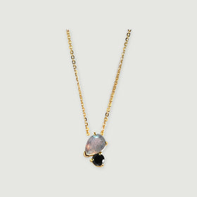 A yellow gold chain leads to a gray pear-shaped stone and a smaller black round stone with polished gold prongs.