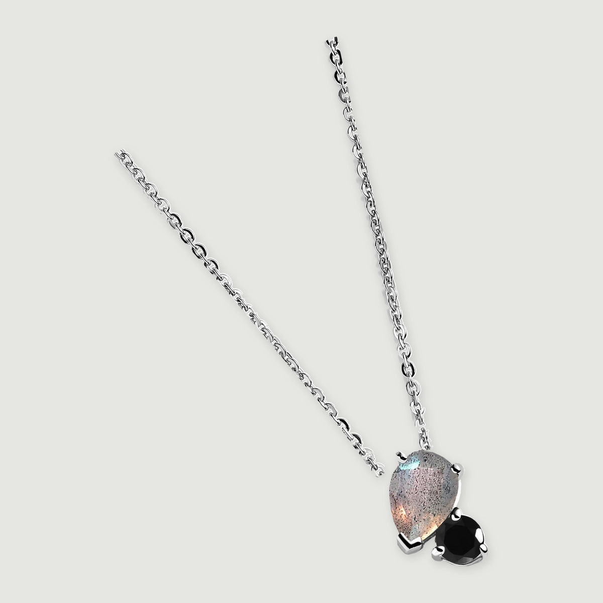 The silver necklace is laid diagonally on a clean gray surface with the two-stone pendant at the lower end.