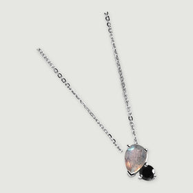The silver necklace is laid diagonally on a clean gray surface with the two-stone pendant at the lower end.