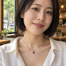 A woman with a short dark bob wears the silver two-stone necklace with a white blouse beside a cafe window.