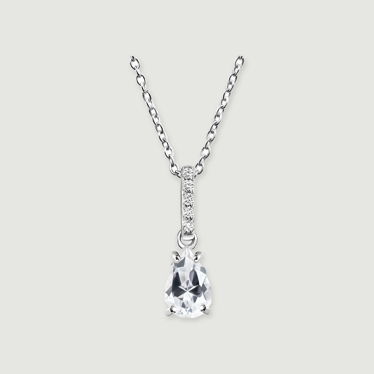 A silver necklace has a clear pear-shaped pendant beneath a narrow bar of five round stones on a light grey background.