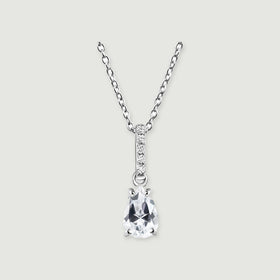 A silver necklace has a clear pear-shaped pendant beneath a narrow bar of five round stones on a light grey background.