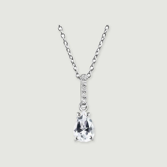 A silver necklace has a clear pear-shaped pendant beneath a narrow bar of five round stones on a light grey background.