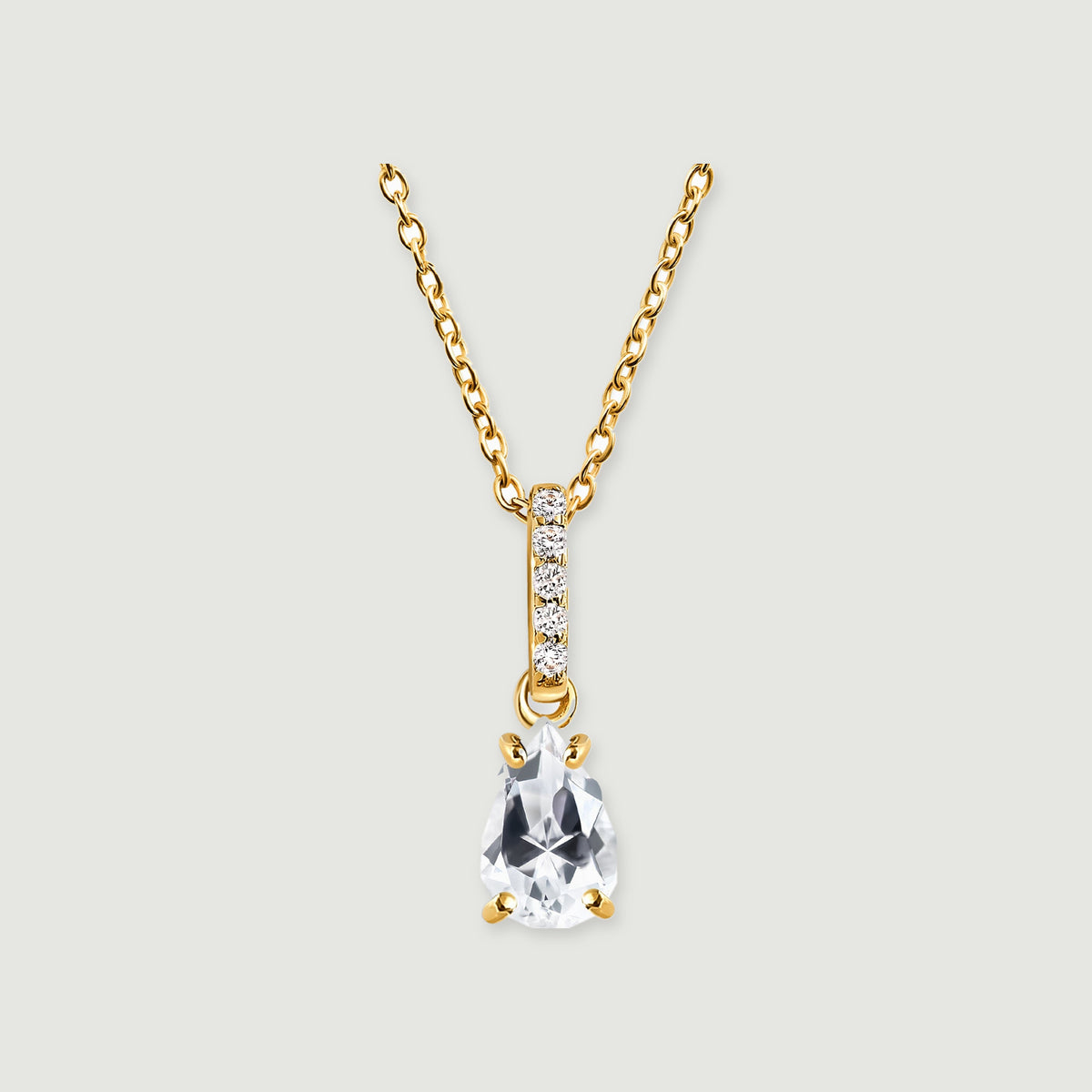 A yellow gold necklace shows a faceted clear drop and a stone-set bail centred against pale grey.