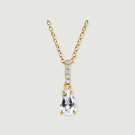 A yellow gold necklace shows a faceted clear drop and a stone-set bail centred against pale grey.