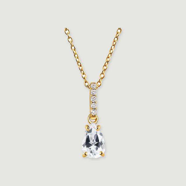 A yellow gold necklace shows a faceted clear drop and a stone-set bail centred against pale grey.