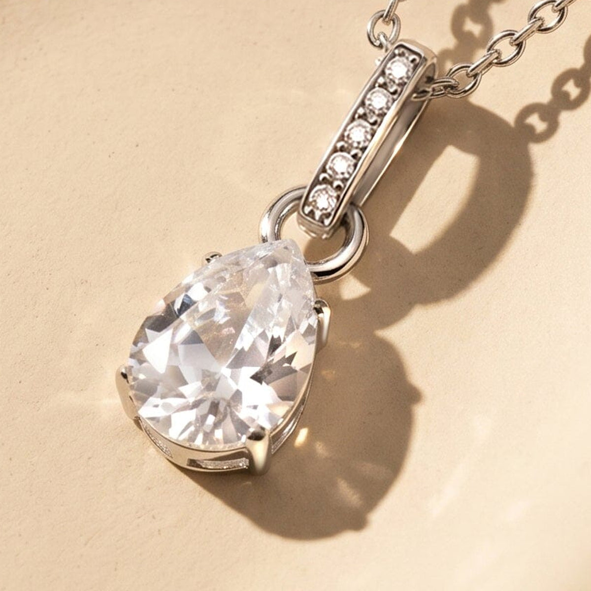 An oblique view shows the clear pear-shaped stone above the silver setting rim and its shadow on a cream surface.