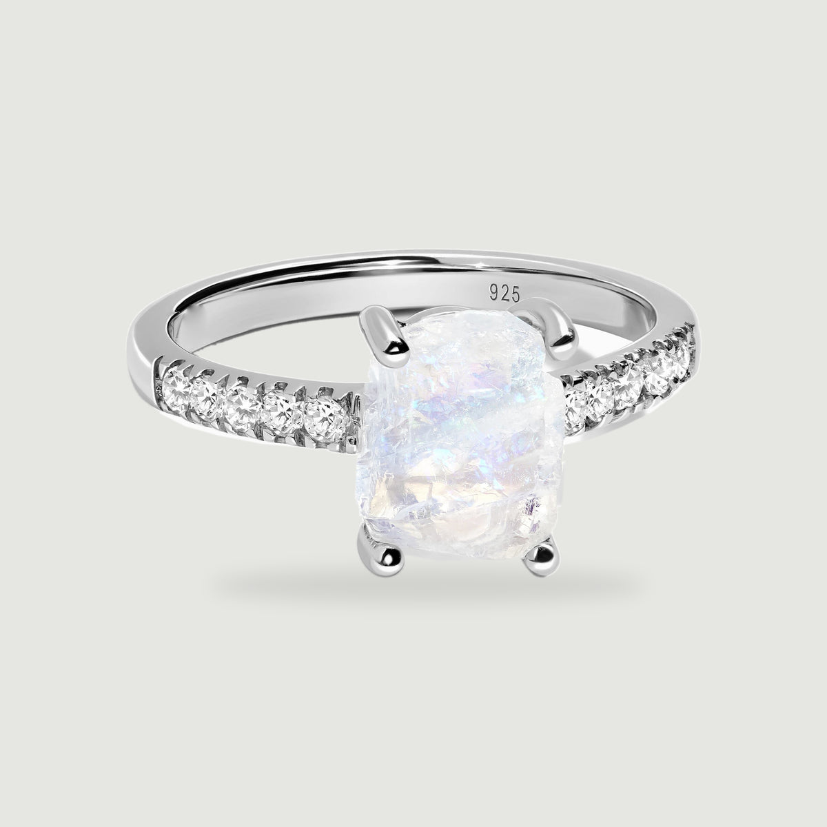 A sterling silver ring displays a rough pale moonstone held by four prongs above a band lined with clear stones.