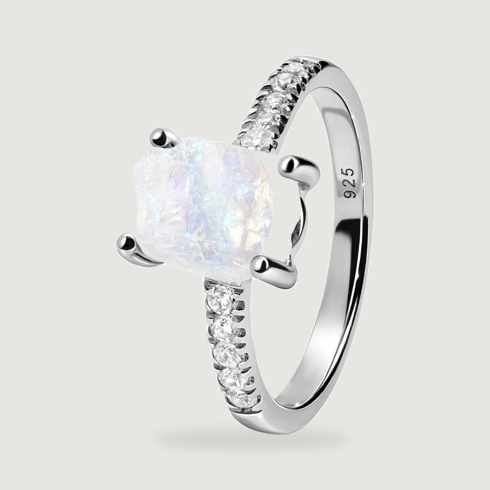 An angled sterling silver ring reveals the raised raw moonstone, curved band, clear shoulder stones, and 925 stamp.