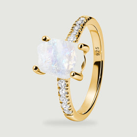 The side of a yellow gold vermeil ring shows rounded prongs, a rough translucent moonstone, and a polished inner band.