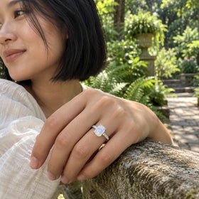 A woman wears a sterling silver moonstone ring while resting her hand on a stone railing in a leafy garden.