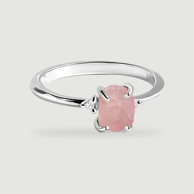 A polished silver ring holds an irregular pink stone between two small clear side stones.