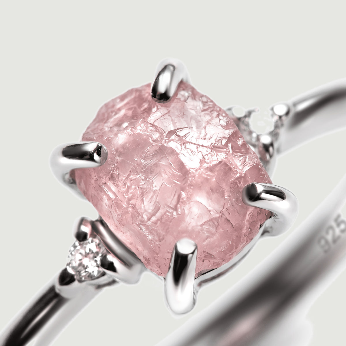 The rough pink crystal and bright silver prongs fill a close view with a clear side stone at the left.