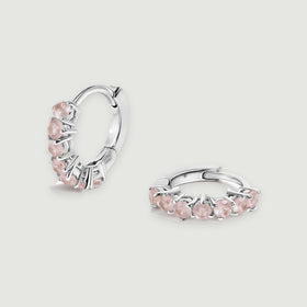 A pair of silver-tone hoops with pale pink round stones rests on a light gray background.