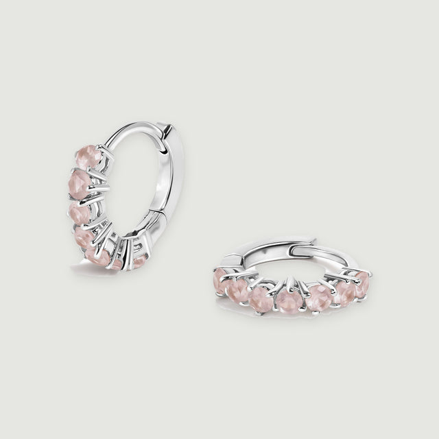 A pair of silver-tone hoops with pale pink round stones rests on a light gray background.