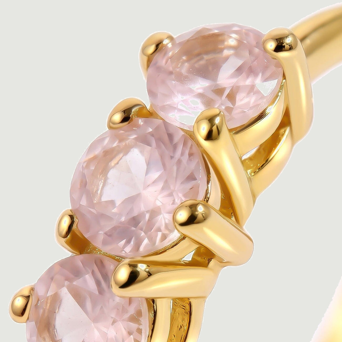 A close view shows faceted pale pink stones held by polished yellow-gold-tone prongs.