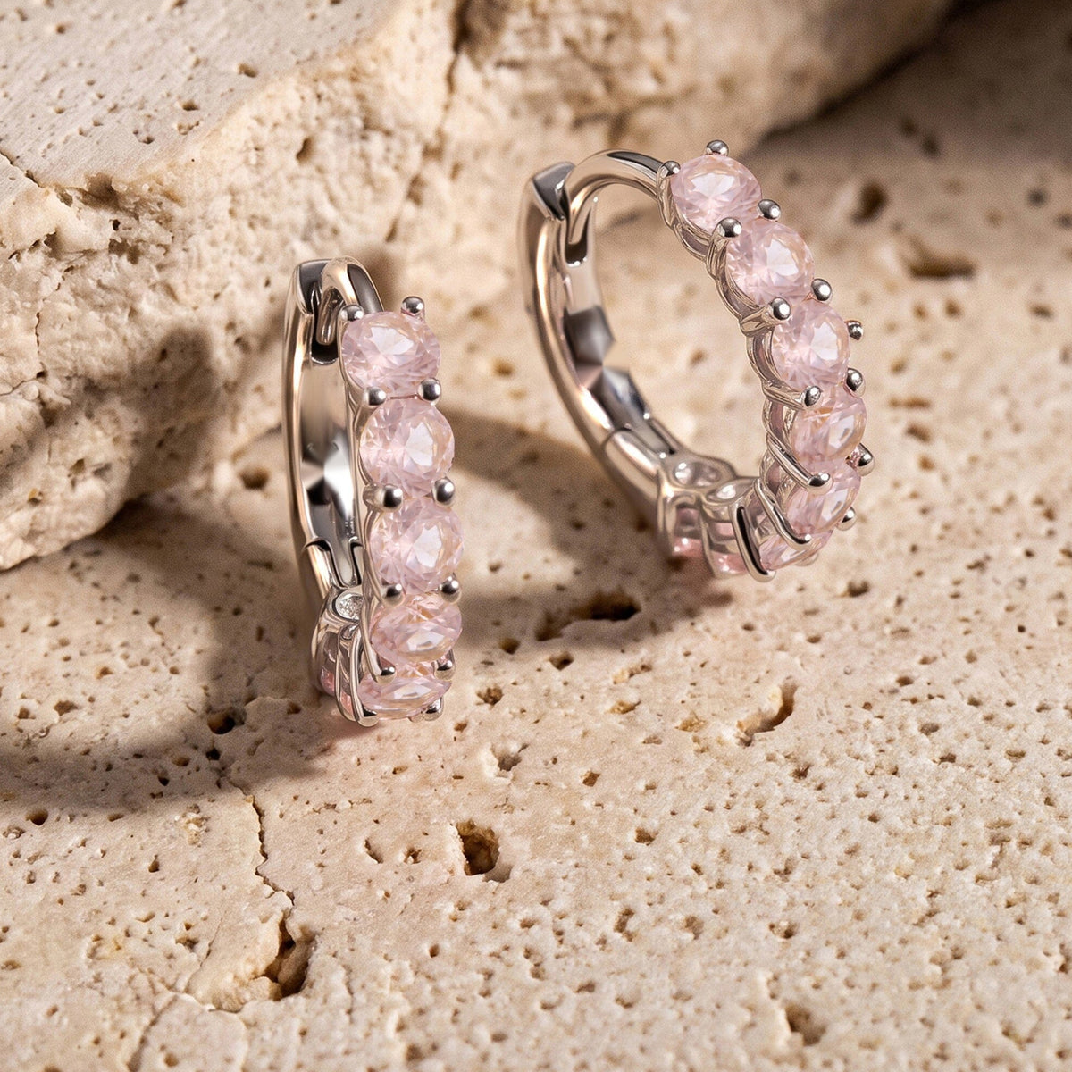 Two silver-tone rose quartz hoops stand beside a textured beige stone ledge.