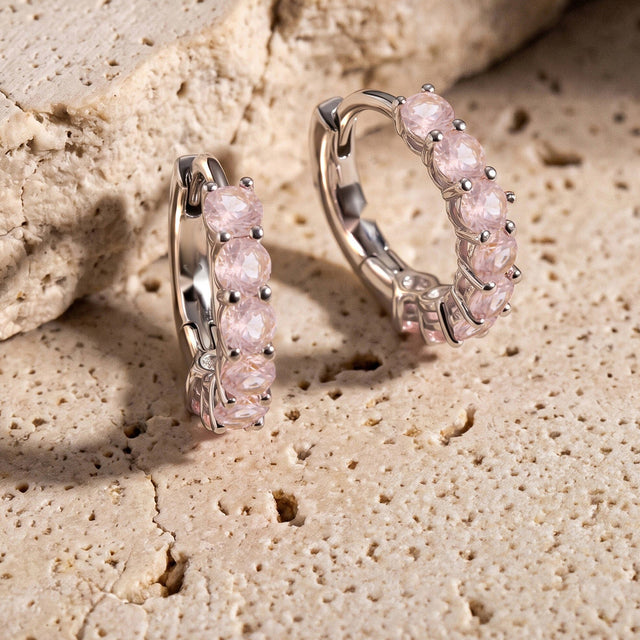 Two silver-tone rose quartz hoops stand beside a textured beige stone ledge.