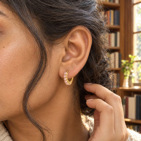 A woman tucks her dark hair behind an ear wearing a yellow-gold-tone rose quartz hoop inside a bookshop.