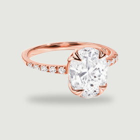 A complete rose gold vermeil ring with an oval clear faceted stone and small stones along the shoulders rests on a light gray background.
