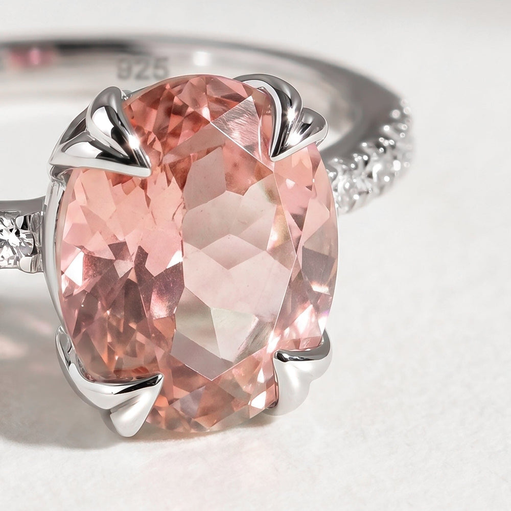 A close view shows a pink oval faceted stone held by four silver prongs with small clear stones beside it.