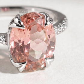 A close view shows a pink oval faceted stone held by four silver prongs with small clear stones beside it.