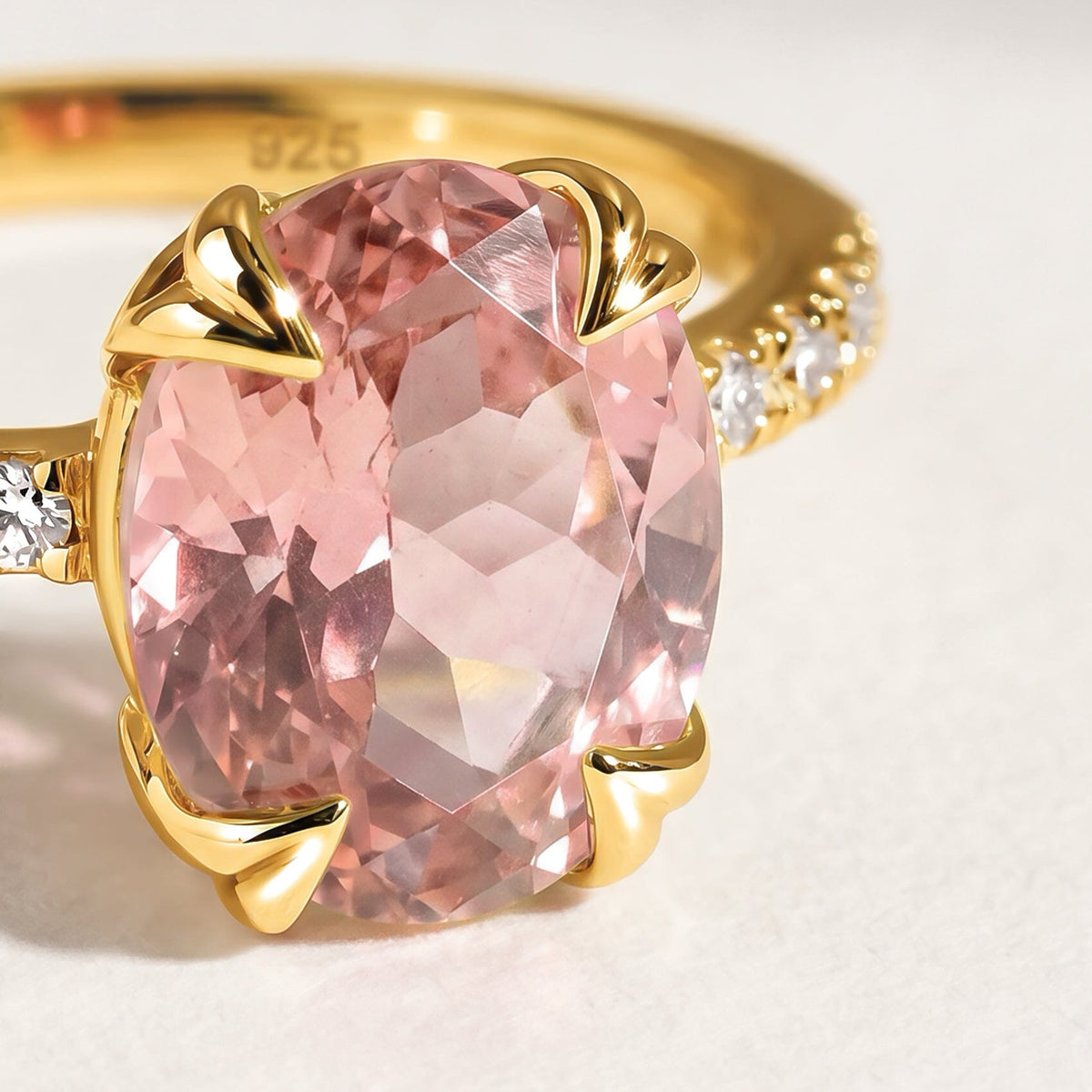 The pink oval stone and polished yellow gold prongs appear in close focus above a pale tabletop.