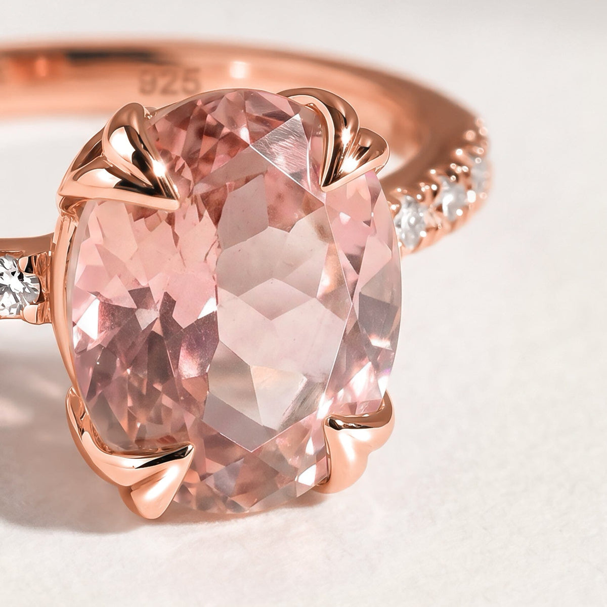 Four rose gold prongs frame a pink faceted oval stone with clear accent stones along the curved band.