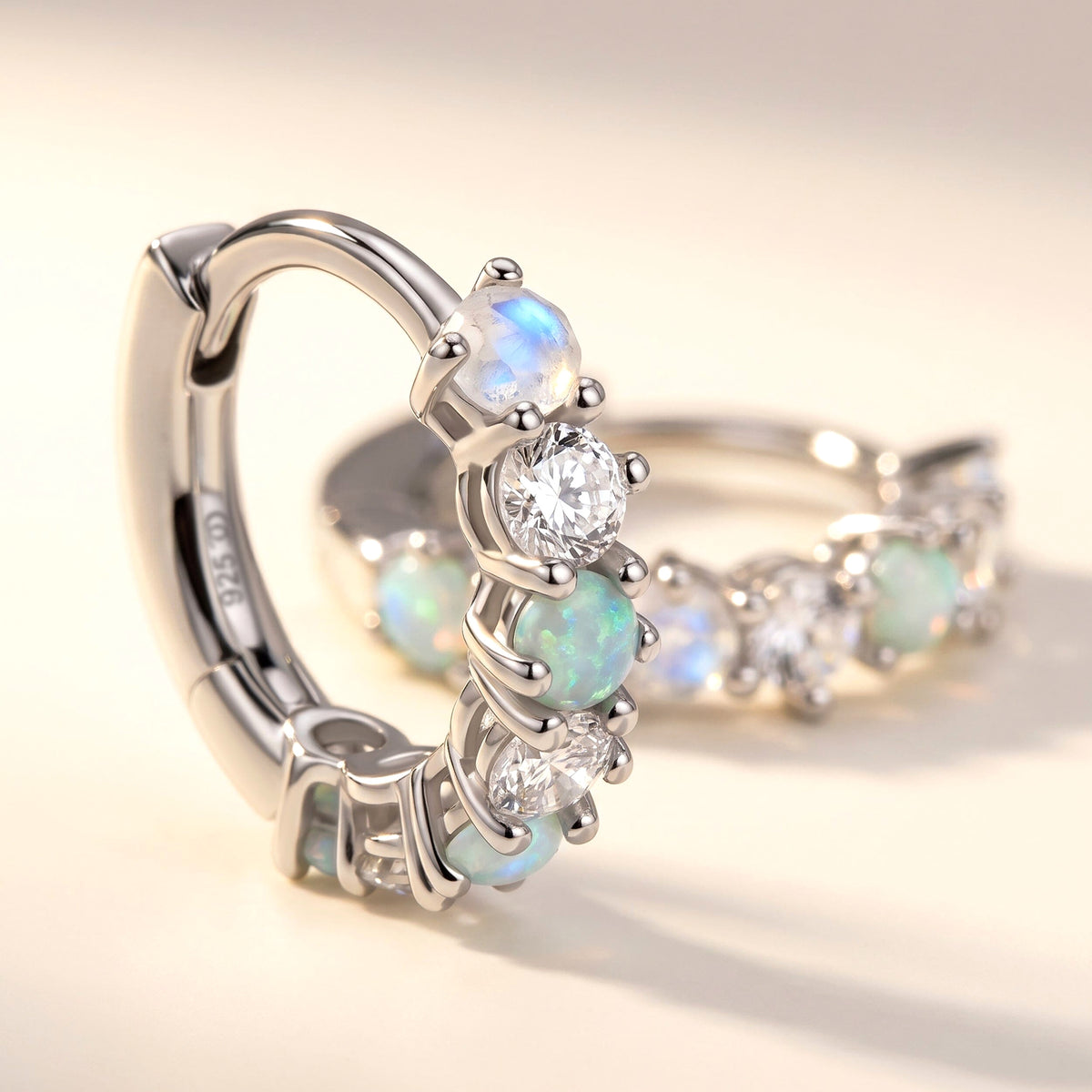 A close view of a sterling silver hoop shows polished prongs and round stones on a clean ivory tabletop.