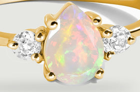 A close view shows the opal color flashes, rounded gold prongs and two clear side stones.