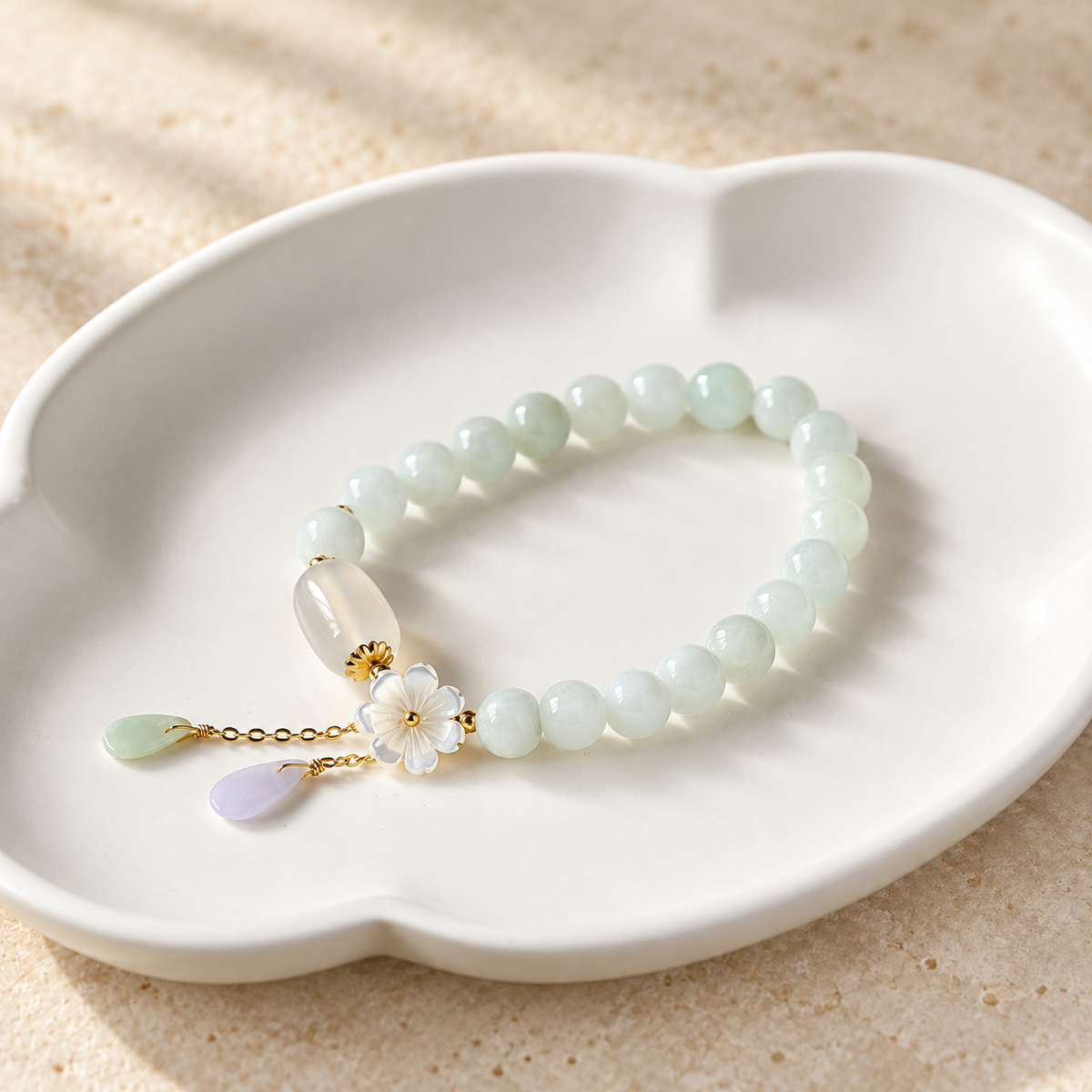 White jade bead bracelet with a flower charm and two drops on a white dish.