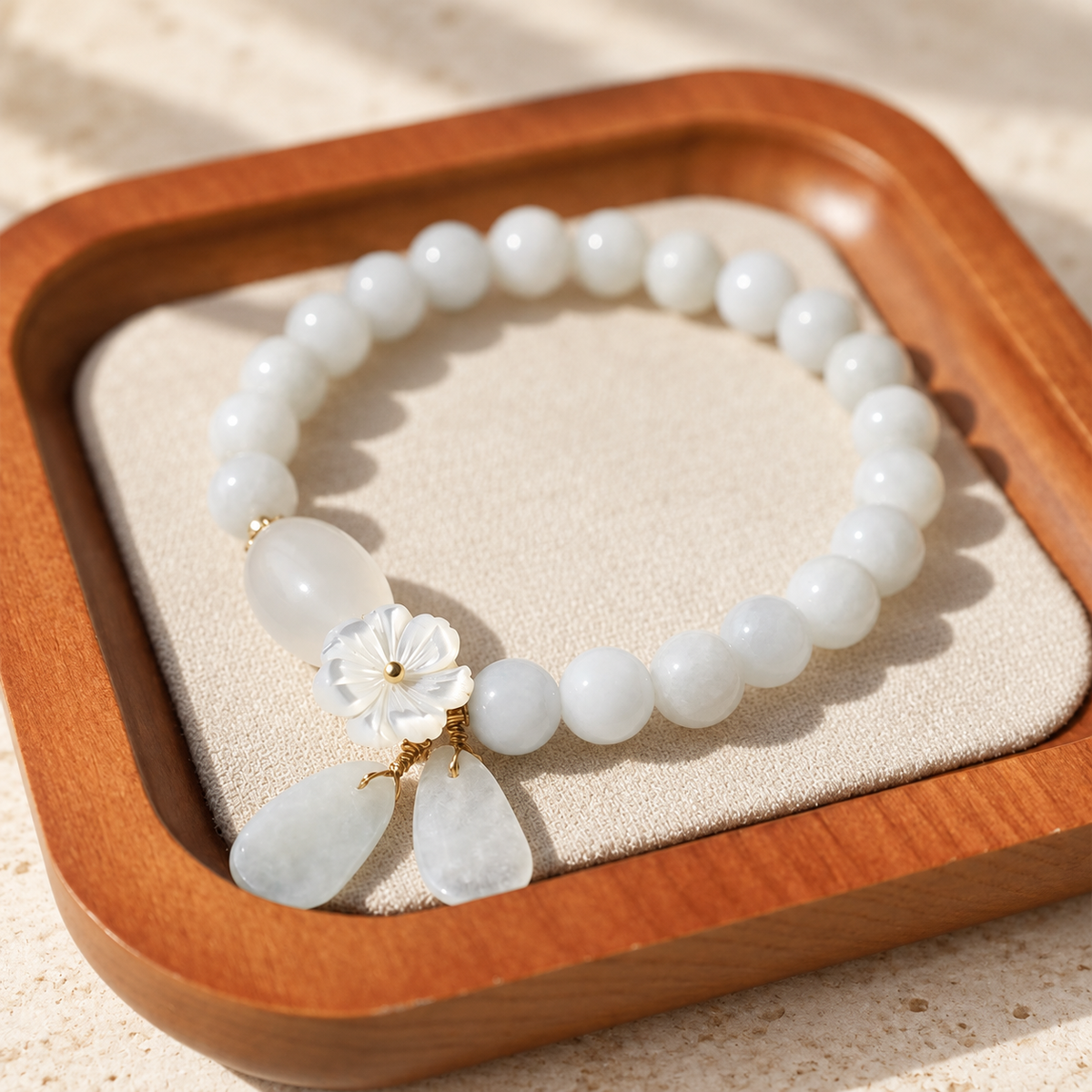 White jade bead bracelet shown from above on a tray, with flower and drop details.
