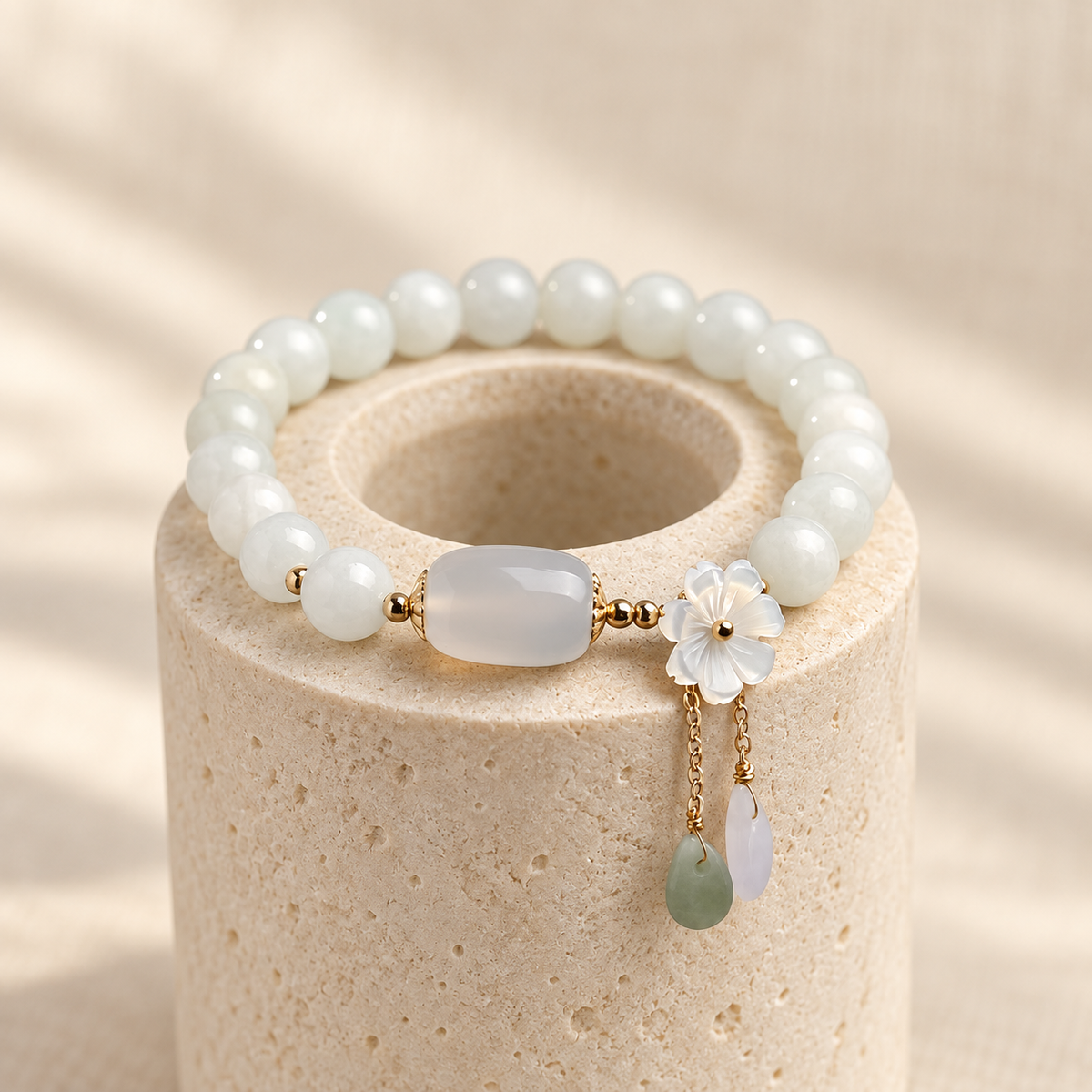 White jade bead bracelet on a ring stand with its carved flower and two drops.