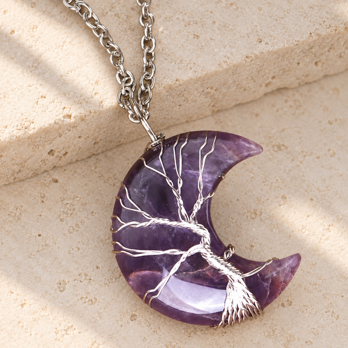Purple crescent pendant with a silver-toned wire tree, shown in a close-up.