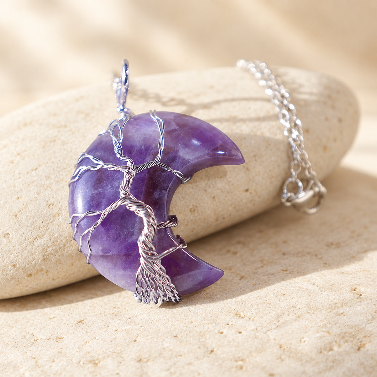 Purple crescent pendant resting against a stone with its chain visible.
