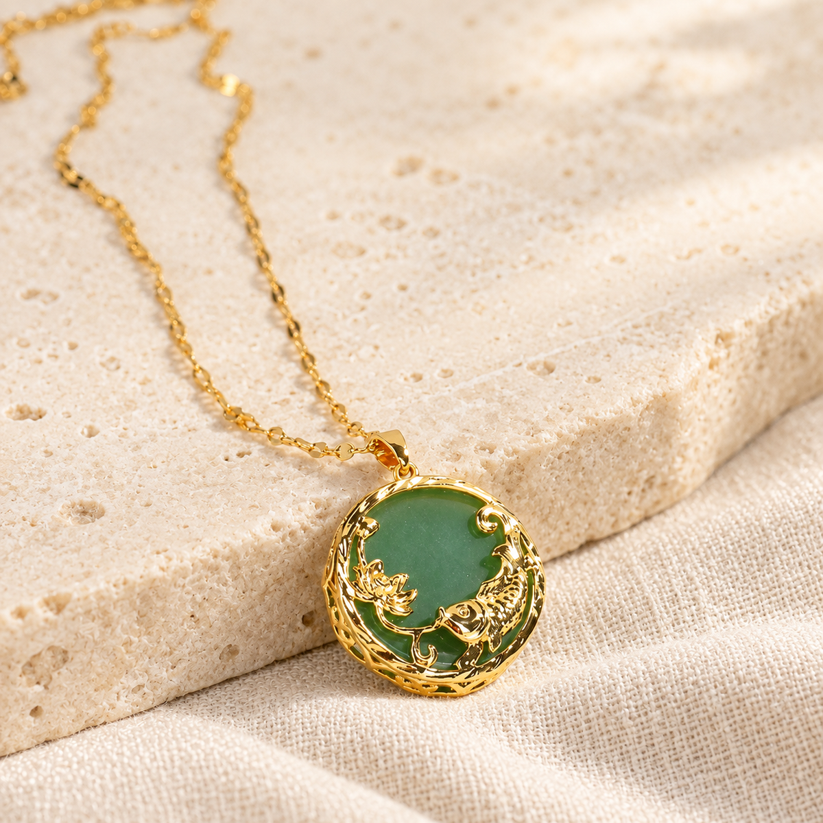 Green circular pendant with a gold-toned koi and lotus motif beside its chain.