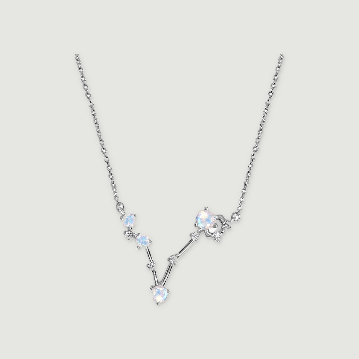 A silver necklace has four round pale stones and small clear accents connected in a V-shaped setting on a light gray background.