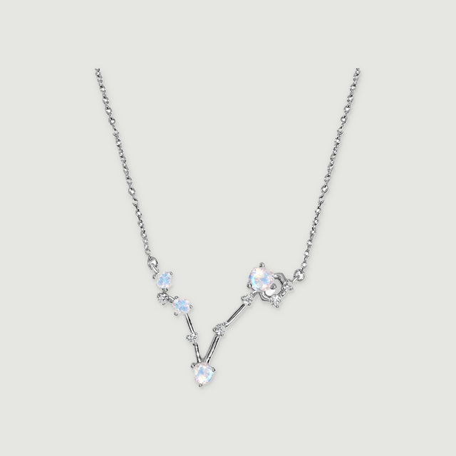 A silver necklace has four round pale stones and small clear accents connected in a V-shaped setting on a light gray background.